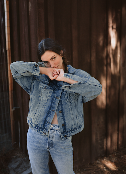 woman wearing denim jacket and jeans against wood panel wall
