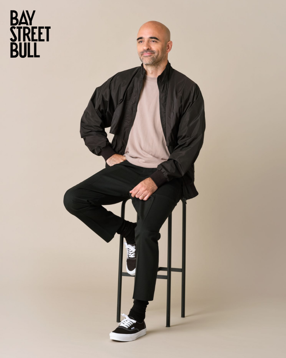 SSENSE Rami Atallah wearing black jacket, beige t-shirt and black pants and sneakers on a stool