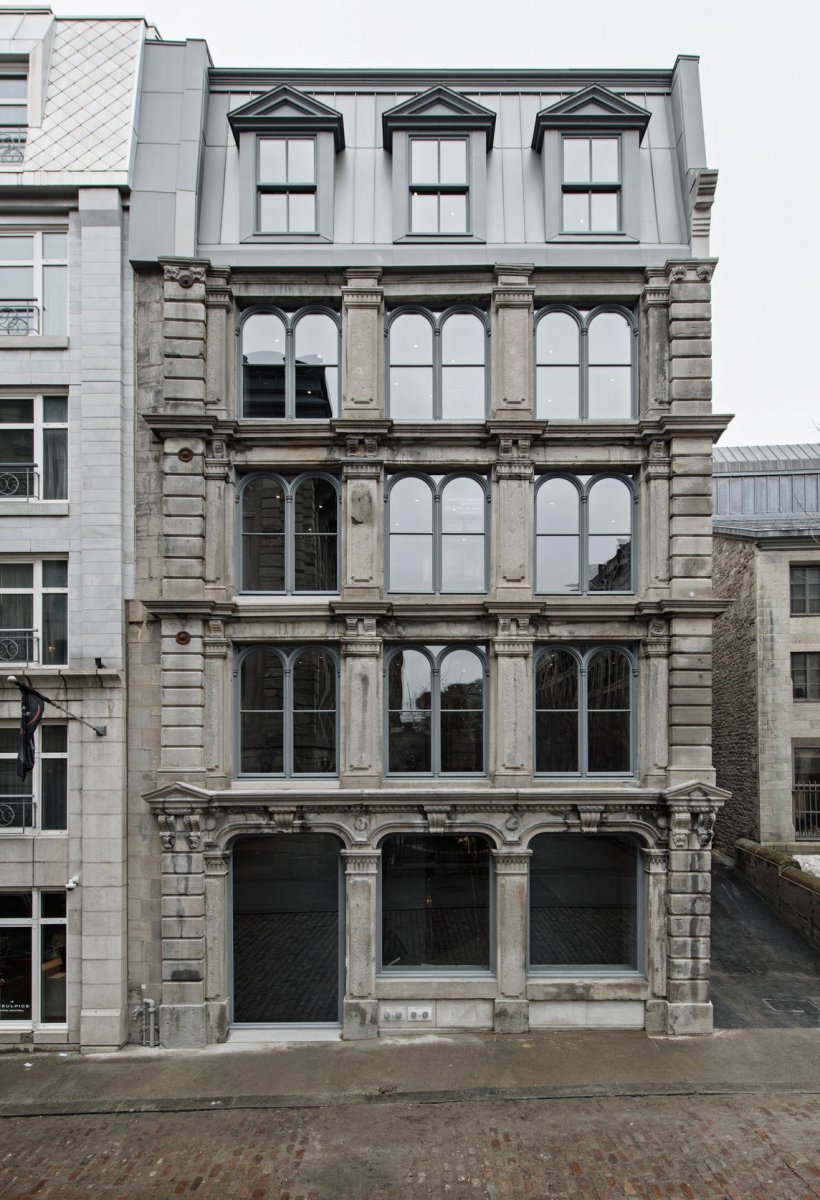 SSENSE historic building made of grey stone with gleaming windows on cobble stone road